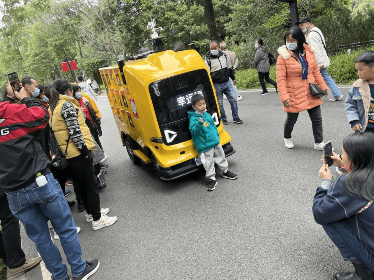 游客争相与停下的无人车合影留念
